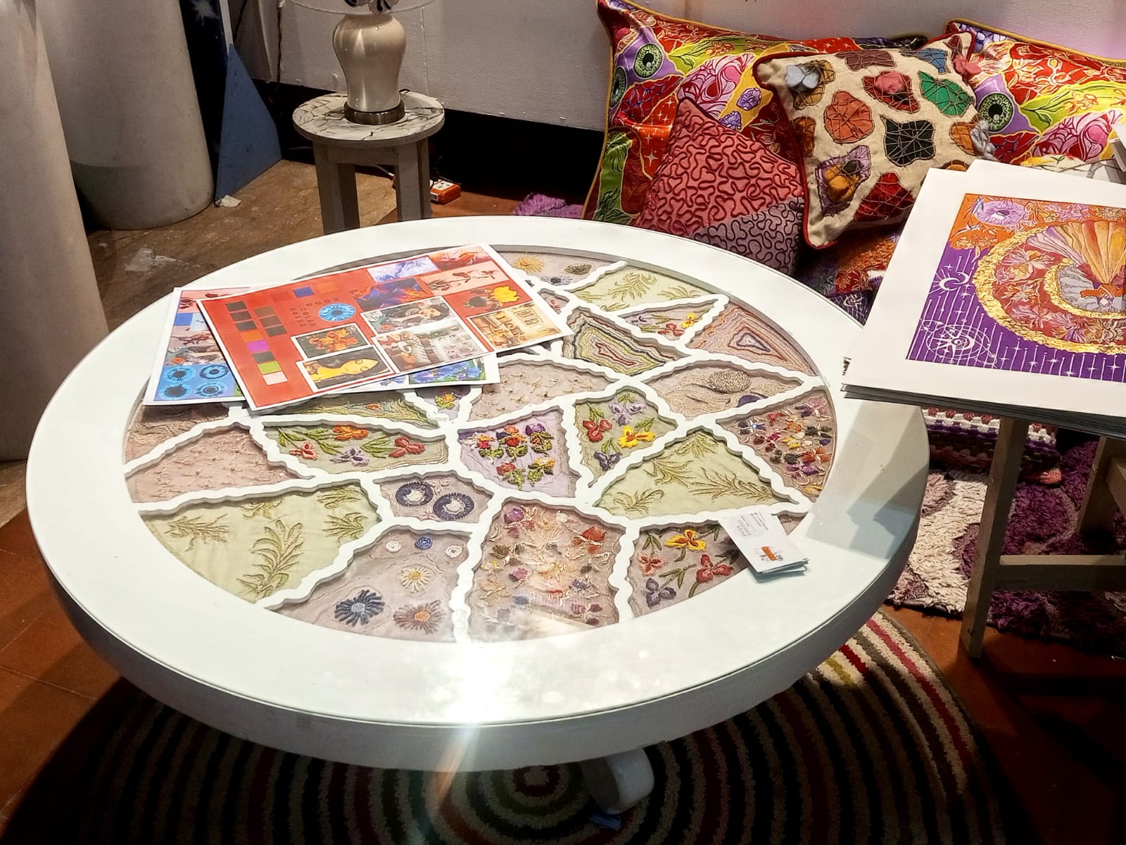 Studio table with an embroidered circular textile piece, mood boards and cushions
