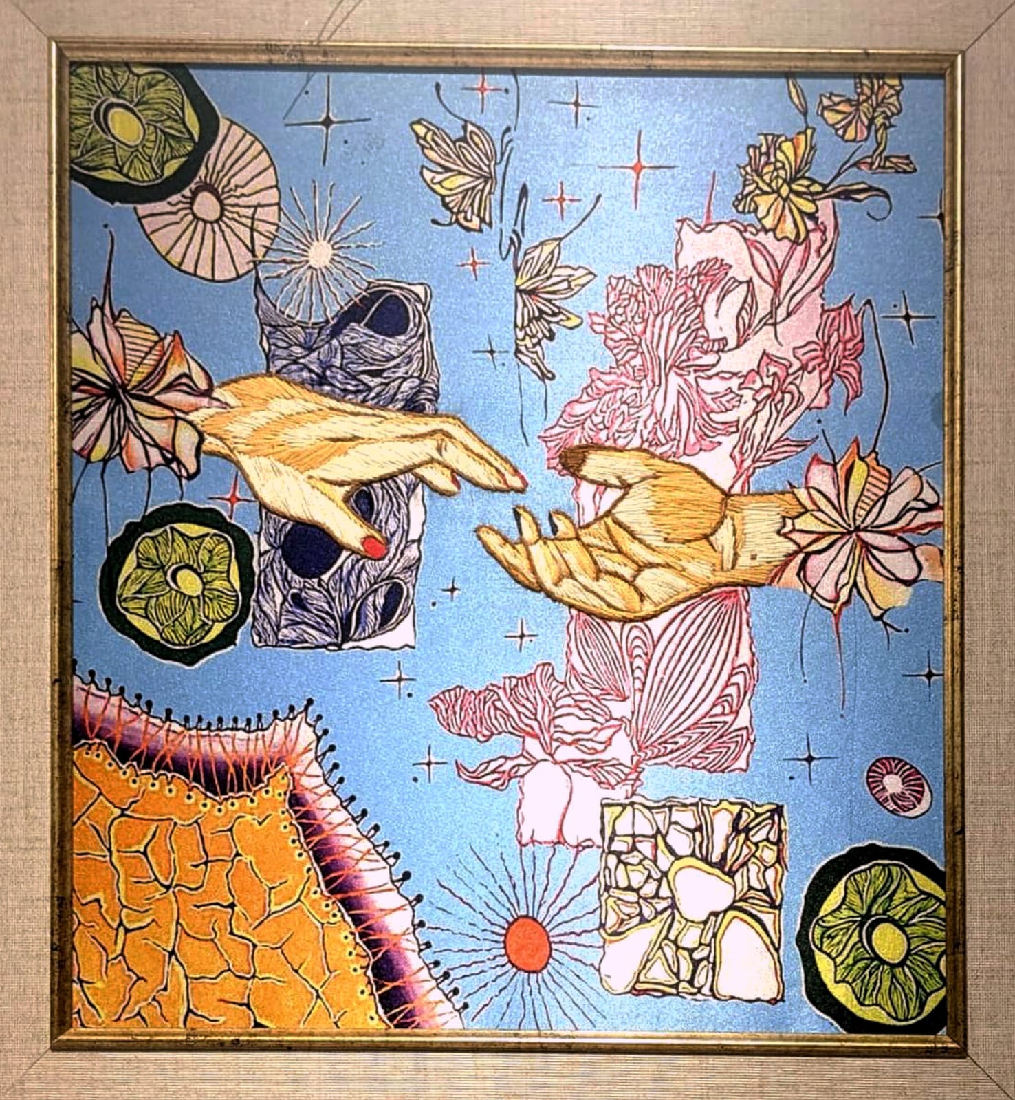 Framed piece of two reaching hands on a blue ground with flowers and stars